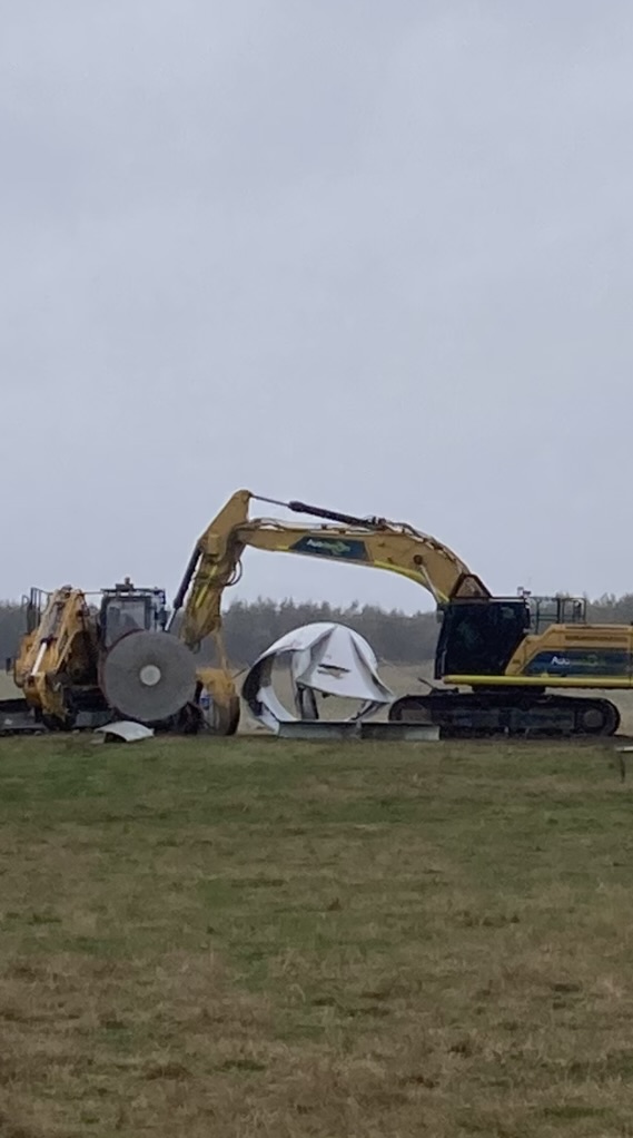 Machinery positioned beside sections of a wind turbine blade during processing activity
